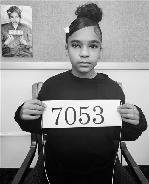 Black and white photo of a female student posing with in same iconic mug shot as Rosa Parks.
